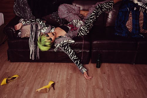 Free Tired transsexual man with bright hairstyle and makeup in fashionable clothes resting on leather sofa after party Stock Photo
