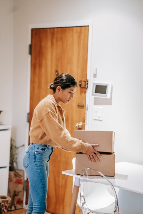 Free Side view of concentrated female in casual clothes preparing cardboard boxes for delivering Stock Photo