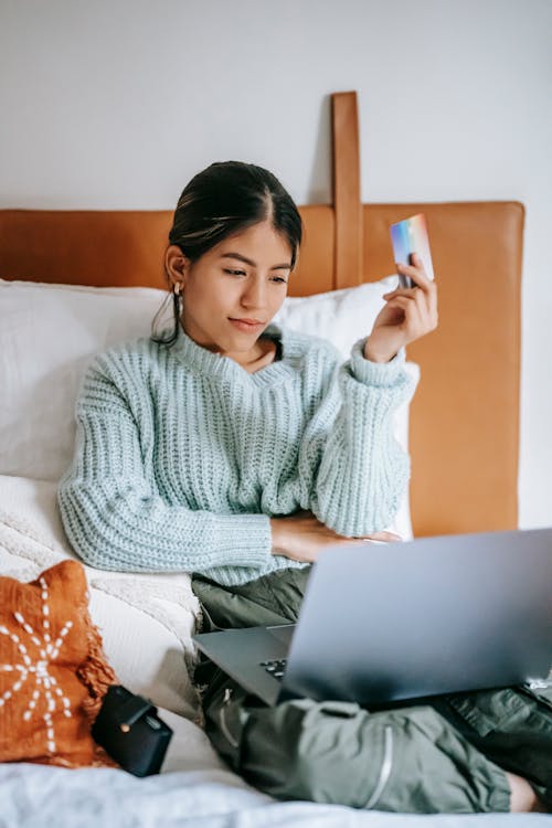 Free Positive Asian woman making online purchase on bed Stock Photo