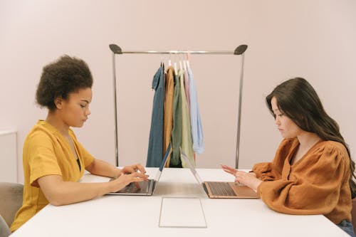 Free A Side View of Women Sitting Near the Table while Typing on Their Laptop Stock Photo